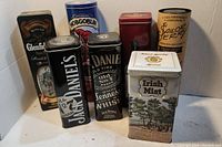 Eight collectible empty tins featuring alcohol branding such as Jack Daniel's, Glenfiddich, Hobgoblin, Irish Mist, and Sailor Jerry.