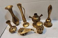 Photo showing all six copper and brass items including vases, oil lamp, vessel, container, and bell arranged in a group.