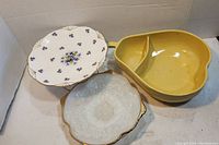 Photo of three pieces of dishware including yellow pear-shaped divided dish and two decorative plates with floral and gold accents.