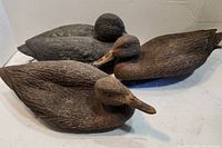 Three carved wooden duck decoys arranged on a white surface showing detail of the feathers and paint.