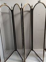 Front angled view showing all four hinged panels of the brass fireplace screen with mesh inserts and arched tops.