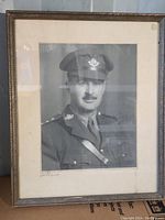 Framed black and white portrait of a WWII soldier in uniform, in a simple gold-tone frame with off-white matte. Signed bottom left of photo.