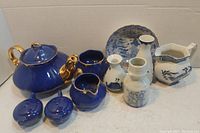 Front view of all glassware items including blue ceramic teapot, sugar bowls, creamers, porcelain vases, pitcher, and plate
