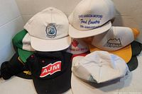 Photo showing front view of the collection of company and promotional hats stacked together, highlighting logos of Charles Concept, Dave Landon Motors Ford Country, Deakin, and AJM.