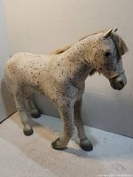 Full side view of large speckled horse toy figurine against plain background.