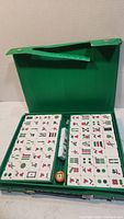 Open green carrying case revealing the full Mah Jong tile set and dice inside.