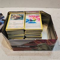 Two stacks of Pokemon cards inside Tyranitar tin box showing front sides of cards including Kangaskhan and Energy card