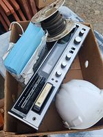 Box with vintage audio receiver with cassette deck, spool of black cable and stack of blue envelopes or booklets inside