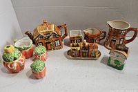 Front view of tea set including cottage-themed teapot, creatmers, cottage salt/pepper shaker and three pumpkin shakers.