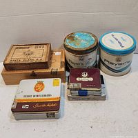 Front angle view of the entire collection showing various vintage cigarette tins and wooden cigar boxes arranged together.