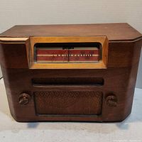 Front view of vintage tube radio with wood cabinet, dial window with frequency markings, two control knobs and speaker grille.