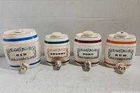Front view of all four ceramic barrel decanters labeled Gin, Sherry, Port, and Rum with distinct colored bands and spigots.