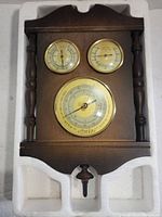 Full view of the walnut weather station showing top decorative edge, side spindle columns, and three instruments.