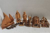 Overview of the lot showing sailboat, fisherman and fisherwoman figures, animal carvings, and two crab catcher cages with one incomplete