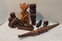 View showing seven carved wood decor items including animals and tribal figures arranged on white background