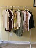 Ten women's size 1X Zara tops hanging on a white clothing rack against a yellow wall, showing colors and styles.