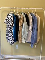 Photo of 10 tops hanging on a rack including striped, blue, beige, black, white tops.