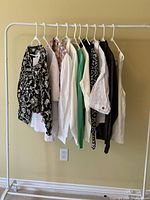 Photo of 10 women's tops hanging on rack showing variety of colors and styles.