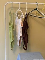 Three one-piece swimsuits hanging on a rack, colors light green, white, and dark brown visible.