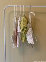 Five women's tops hanging on rack, showing various colors and styles including green knitted top and white camisole