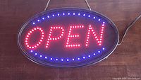 Front view of the illuminated LED open sign on a wooden surface showing the red 'OPEN' text and blue border lights.