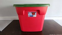 Front view of red plastic storage container with green snap-on lid, showing label.