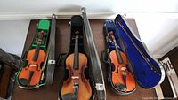 Three violins in open cases showing interior colors green, black, and blue along with bows