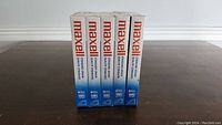 Five new Maxell VHS tapes, sealed and standing upright, showing the front and side box design with brand and recording time.