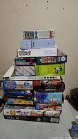 Stacked view of board games, puzzles, science kits, and books showing titles and variety of items in the lot
