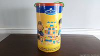 Cylindrical container of Imaginarium wooden building blocks, showing branding and images of children playing with blocks.