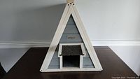 Front view of triangular A-frame pet house with small entry and awning.