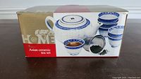 Box showing front of the ceramic tea set with teapot and multiple tea cups in white with blue pattern.