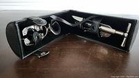 Open black leather case showing all the accessories including corkscrew, foil cutter, and wine stopper inside.