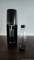 Front view of black Sodastream soda maker beside reusable carbonating bottle on table.