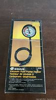 Photo of the packaged Equus Vacuum/Fuel Pump Tester showing the gauge, hose, and product information on the box.