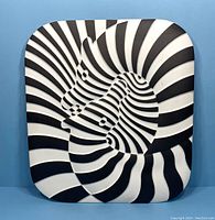 Straight-on view of square porcelain plaque featuring embossed black and white zebra stripe pattern forming zebra head design.