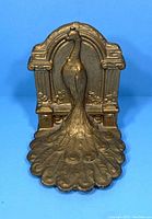 Front view of brass bookend with detailed peacock design and arched backdrop.