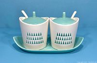Front view of vintage Horishin Ware condiment set with two ceramic jars, lid, spoons, and tray against blue background
