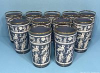 Eleven blue highball glasses arranged in rows showing white Hellenic figures and gold rims