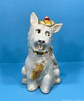 Front view of vintage white Scottie Terrier coin bank with hat, scarf, and shield emblem on chest.