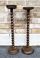 Pair of vintage wooden barley twist ashtray stands side by side against brick wall showing full height and design.