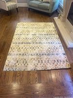 Area rug laid out on hardwood floor in front of furniture, showing top and side angles with geometric diamond designs.