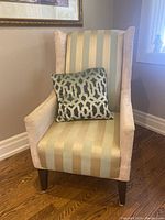 Front view of wingback upholstered armchair with light striped fabric and decorative pillow on seat.