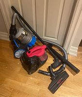 Pair of two Bissell vacuum cleaners placed on floor with hoses and attachments