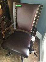 Full view of the Bombay Company leather office chair with wood frame, showing the seat, backrest with nailhead trim, armrests, and caster base.