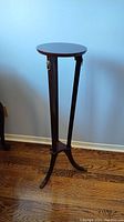 Full view of the tall wooden plant stand showing the round top, three legs with metal lion accents, and claw feet