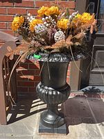 Front angle of the black cast iron planter with faux flowers, showing the full height and decorative floral arrangement.
