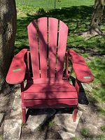 Front view of a red Adirondack chair placed outdoors under a tree.