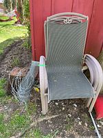 Four stackable outdoor chairs with metal frames and mesh fabric seats and backs, weathered and located outdoors next to a red wooden wall. Small roll of wire fencing placed beside the chairs.
