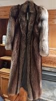 Full view of a vintage raccoon fur coat hanging indoors showing length and natural fur texture.